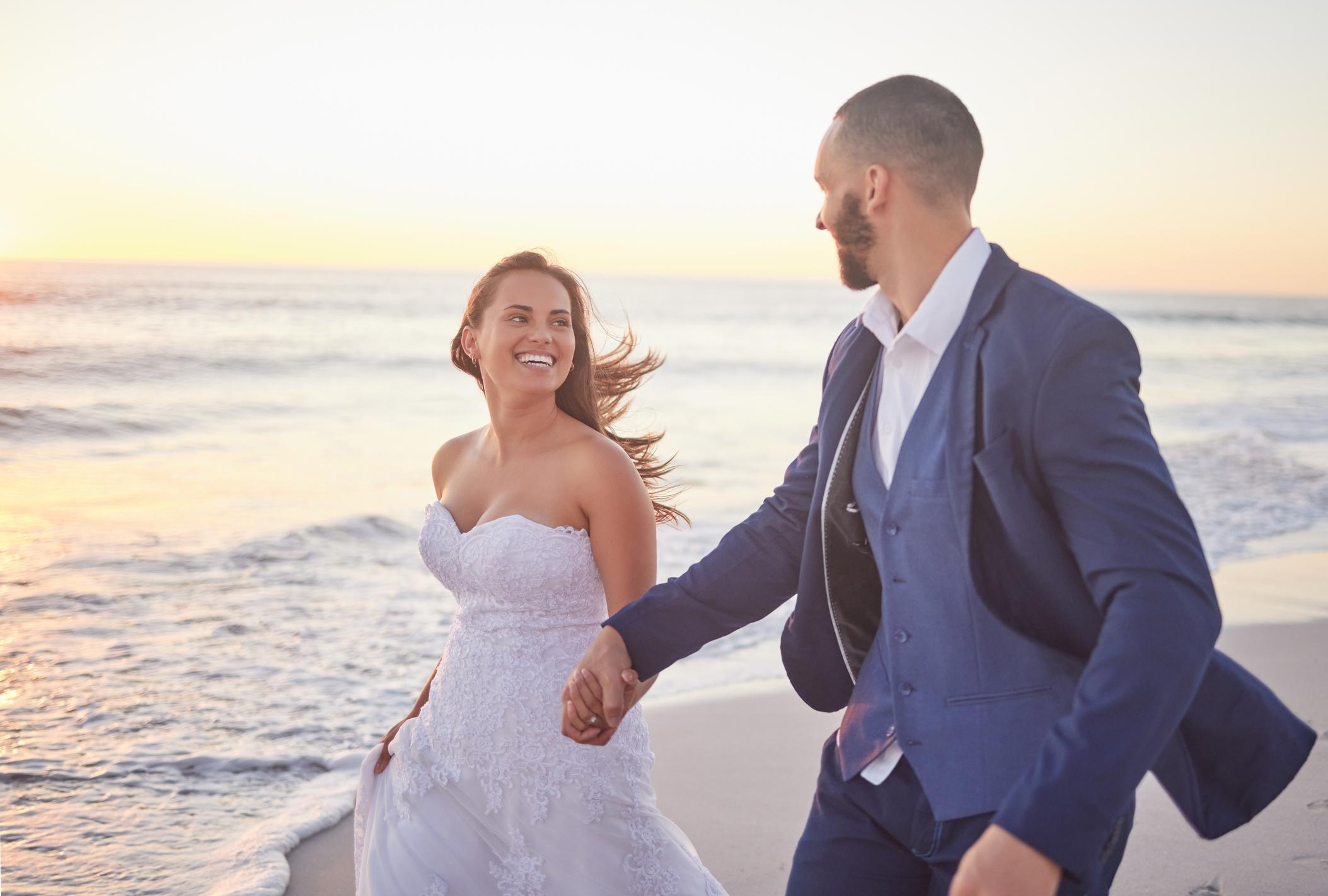 Couple, Wedding And Beach Smile In Sunset On Romantic Walk Together After Getting Married. Happy, Wife And Man In Suit Walking At Ocean, Romance And Marriage After Ceremony With Sun Setting Over Sea